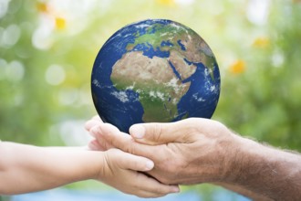 Child and senior man holding planet Earth in hands against green spring background. Elements of