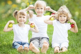 Happy children with fruits sitting on green grass in spring park