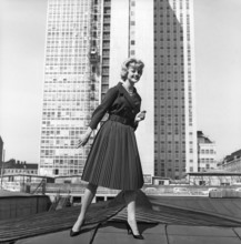 In the 1950s. A woman modelling a 1950s outfit with a jacket and skirt in matching dark. In the
