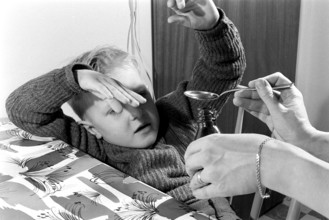 A boy is sick and won't take his medicine. His mother holds out a spoon and waits for him to gape