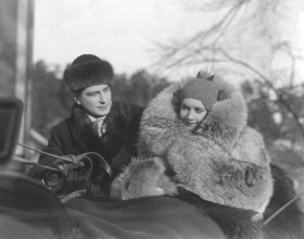 Fur coat in the 1930s. A young couple is sitting together in a horse drawn sledge. The woman is