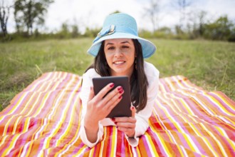 Attractive smiling young woman dressed casually uses e-book/tablet lying down on a colourful