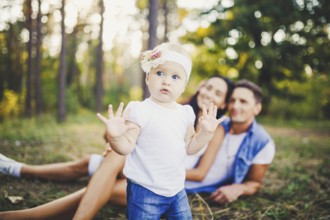 Little girl one year on the background of parents resting on graß learning to walk on nature in the