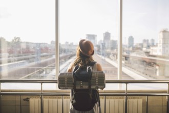 Traveler Rear view woman standing at the window in hall Train Station departure with backpack,