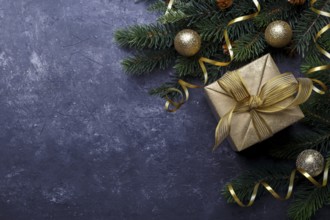 Christmas flat lay with golden gift box and fir tree branch on black stone background with copy