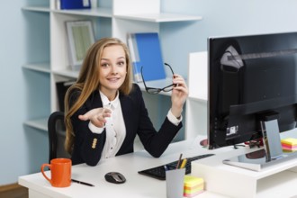 Young pretty business woman sitting at the desk with computer in blue office