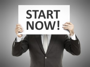 A business man holding a paper in front of his face with the text start now