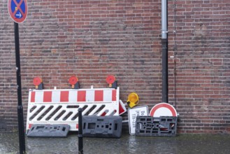 Red and white construction barrier, traffic signs, and bases stacked against a brick wall with no