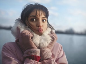 Portrait of a cute lady with a kiss, with bangs, in a pink jacket on the background of the river