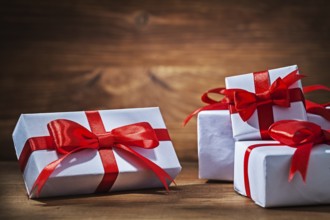 White giftboxes with red ribbons on vintage wood