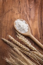 Wooden spoon with white flour and ears of wheat rie on vintage board