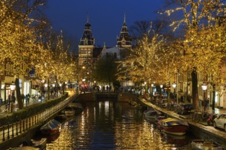 Illuminated canal and bridge at night, surrounded by trees and historic buildings, Amsterdam,
