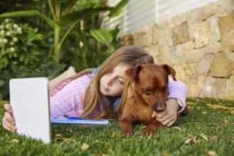 Blond kid girl selfie photo with tablet pc and dog lying on grass