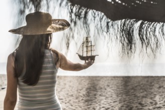 Woman with hat hold boat model on the beach