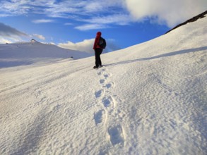 Person walking over snow-covered mountains, clear skies and footprints in the snow, Tromsø, Norway,