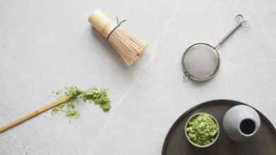 Matcha green tea powder and utensils for drink preparation: traditional bamboo spoon and whisk. Top