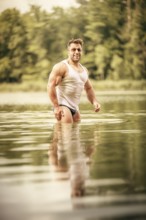 An image of a muscular man in the lake with a white shirt and sunglasses