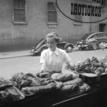 In the 1950s. A woman is pictured in the street and at the storefront of a bakery. She looks as if