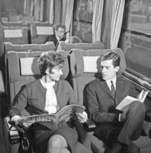 Train travel in the 1960s. A couple on a train, sitting comfortably in the carriage reading a