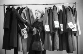 Great discounts of outerwear in the 1960s. A woman stands by a clothes rack, choosing from
