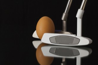 Two different golf putters and egg on a black glass desk