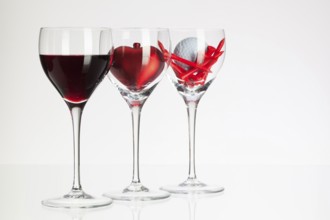 Wine glasses with red wine, heart and golf ball on white table