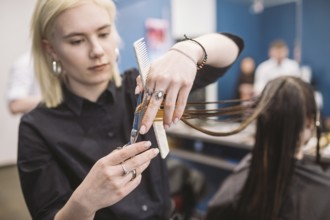 Hairdresser holding scissors and comb and makes haircut woman client. Young beautiful woman hair