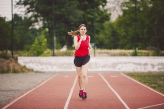 Beautiful young athlete Caucasian woman with big breasts in red T-shirt and short shorts running