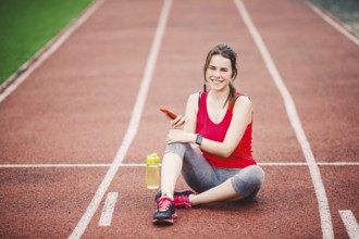 Beautiful fitneß girl uses smartphone at stadium after workout. Sports and healthy. Sport woman use