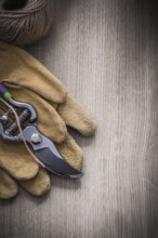 Pair of leather safety gloves sharp metal secateurs and skein of twine on wooden background