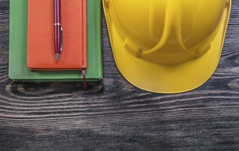 Note-books ballpoint pen protective building helmet on wooden board construction concept