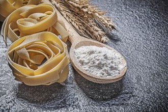 Wheat rye ears wooden spoon flour raw twisted Italian pasta on black background