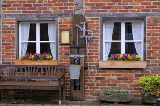 Brick wall with two windows and flower boxes, next to it a wooden bench, gemen, münsterland,