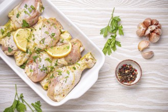 Raw uncooked chicken legs marinated with seasonings, herbs, lemon in white ceramic casserole top