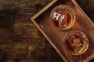 Whiskey in glasses with ice. Bourbon whisky on rocks on a dark rustic wooden background, overhead
