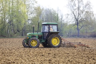 Farmer cultivating field with green John Deere 2140 utility tractor and harrow in the spring. Salo,