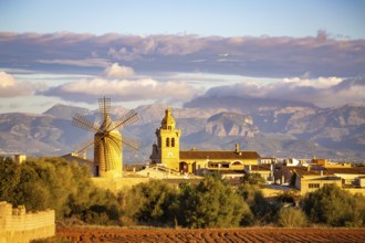 Mountain landscape with village, windmill and church tower under a cloudy sky and flying aeroplane