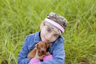 Little girl with pet puppy mascot mini pinscher in outdoor green grass