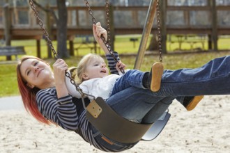 Mother and daughter in a swing having fun at the park playground