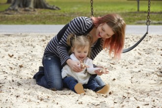 Mother and daughter playing with sand having fun at the park playground
