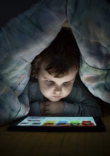 Little girl watching her tablet in the bed. Illuminated child face from device screen. Child