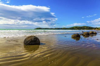 Moeraki's huge round boulders on a sandy beach. The Pacific ocean tide begins in New Zealand. The