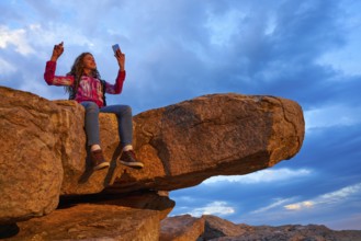 Hiker teen girl selfie smartphone on peak of mountain at sunset