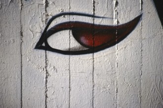 A spray-painted or painted woman's eye with red pupils on a concrete wall