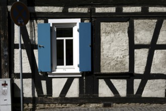 An old rickety half-timbered house with a striking beam construction and shutters at the window