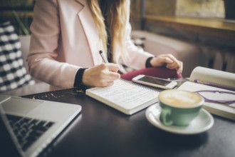 Close up caucasian woman hand on wooden table inside cafe makes notes in notebook. Subject