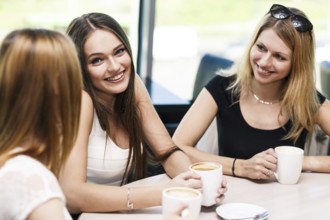 Happy women holding coffee cup while looking at each other in cafe