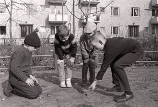 In the 1960s. Boys outdoors playing marbles. An old fashioned game where the goal is to hit the