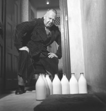 Man of the 1940s. A man visibly disapointed over the several milk bottles standing on his doorstep.