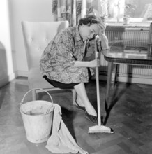 Cleaning the floor back then. A woman looks very tired and worn out when sitting on a chair, having